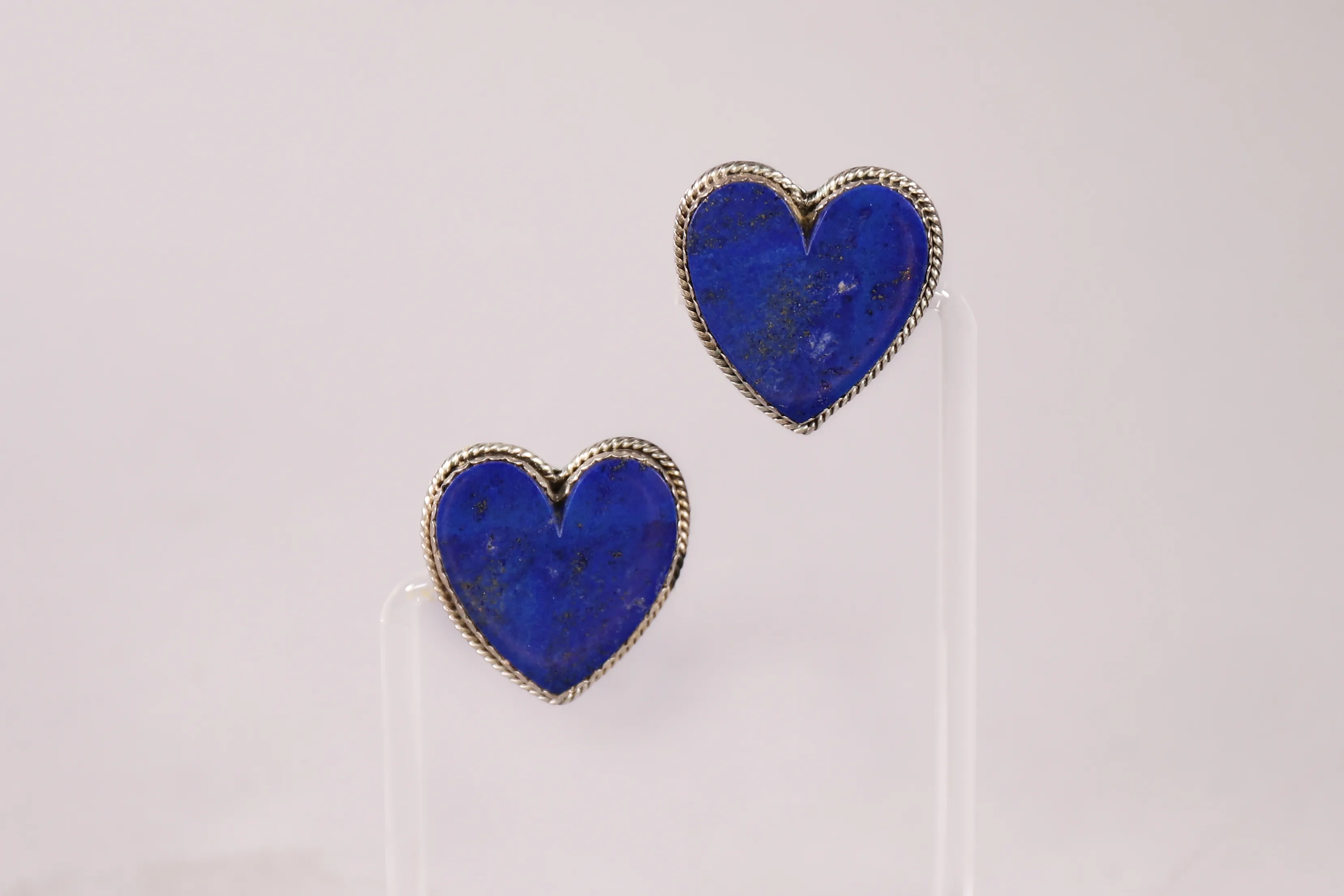 Blue heart-shaped earrings displayed on clear stands.